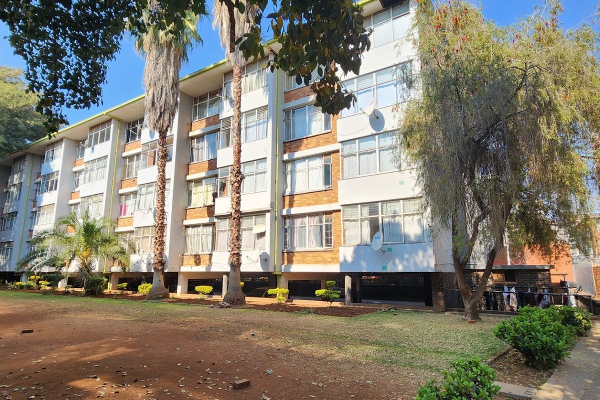 Exterior view of a multi-story apartment building featuring a brick and painted facade with large windows and surrounding landscaped grounds.