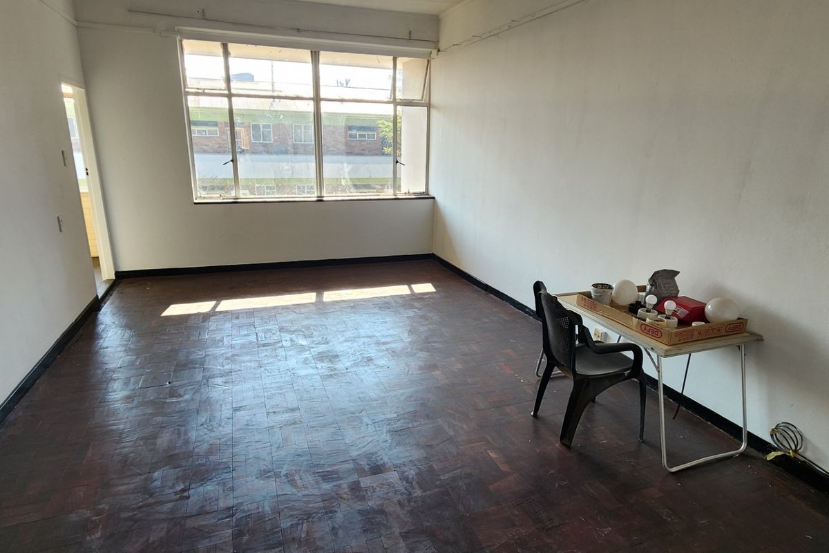 A spacious, empty living area featuring original parquet flooring and a large window, offering a blank canvas for renovation and interior design.