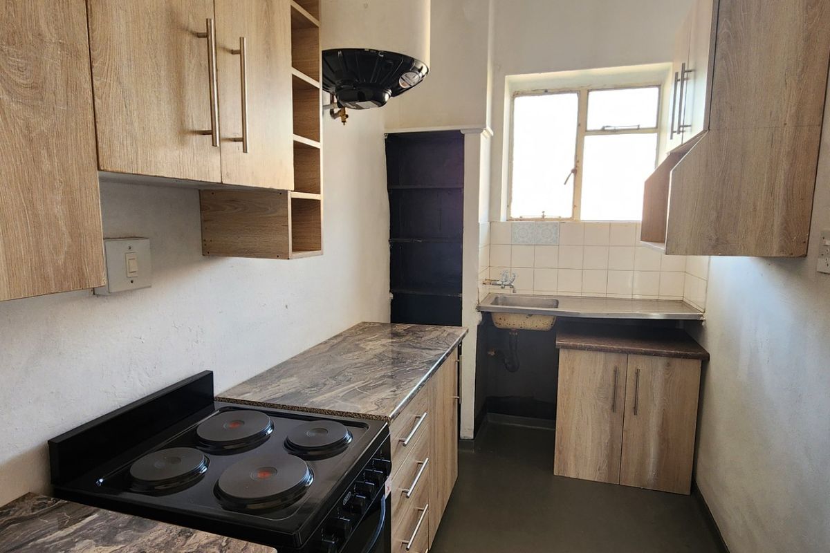 A compact kitchen featuring laminate cabinetry, an electric stove, and a stainless steel sink with tiled splashback, requiring minor cosmetic updates.