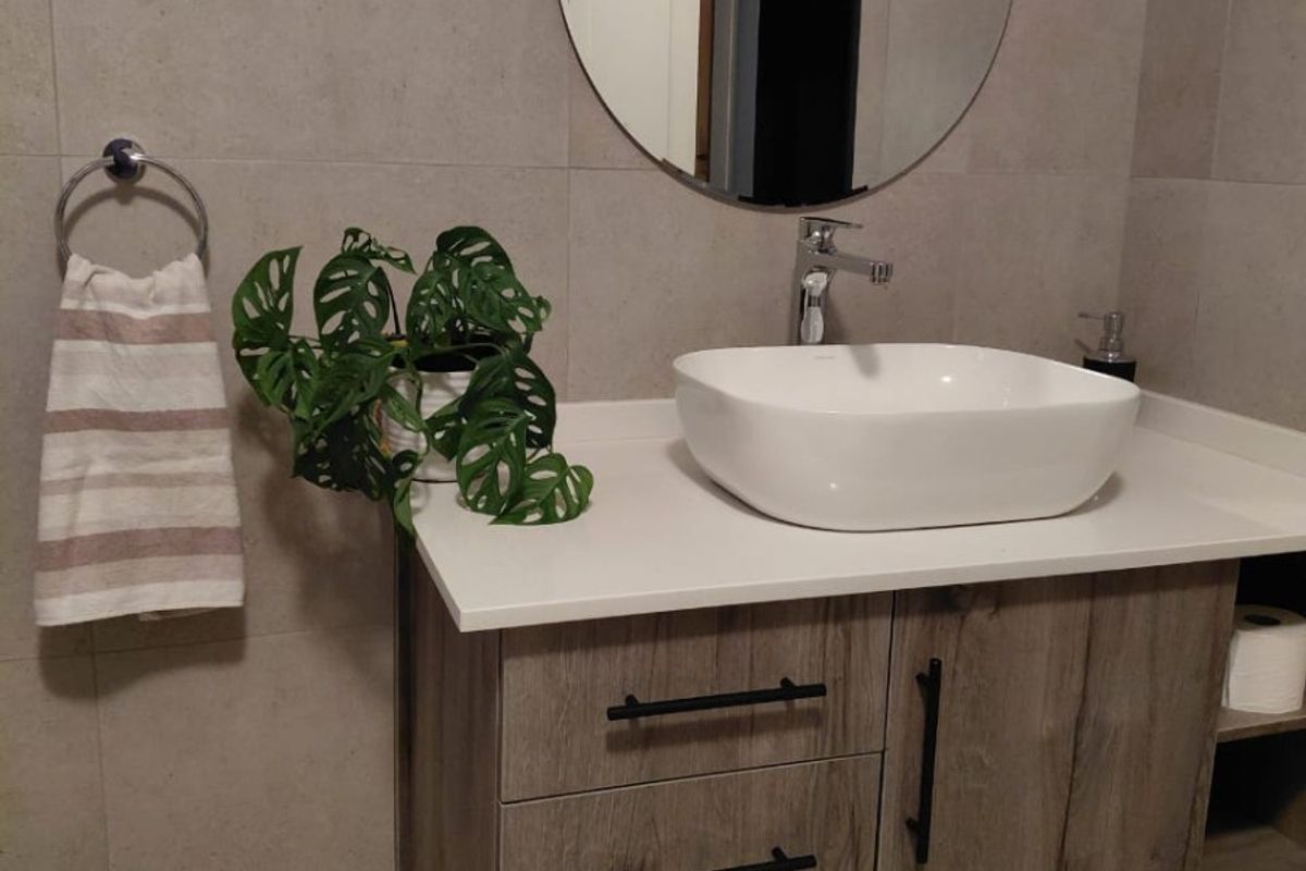 Modern bathroom vanity featuring a vessel sink, wood-grain cabinetry, matte black hardware, and large format wall tiles.