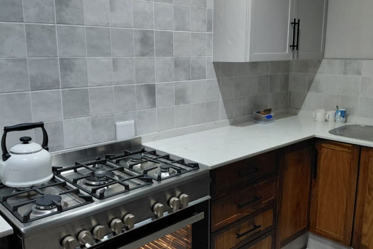 A modern kitchen featuring a stainless steel gas stove, quartz countertops, tiled backsplash, and a mix of light and wood-toned cabinetry.