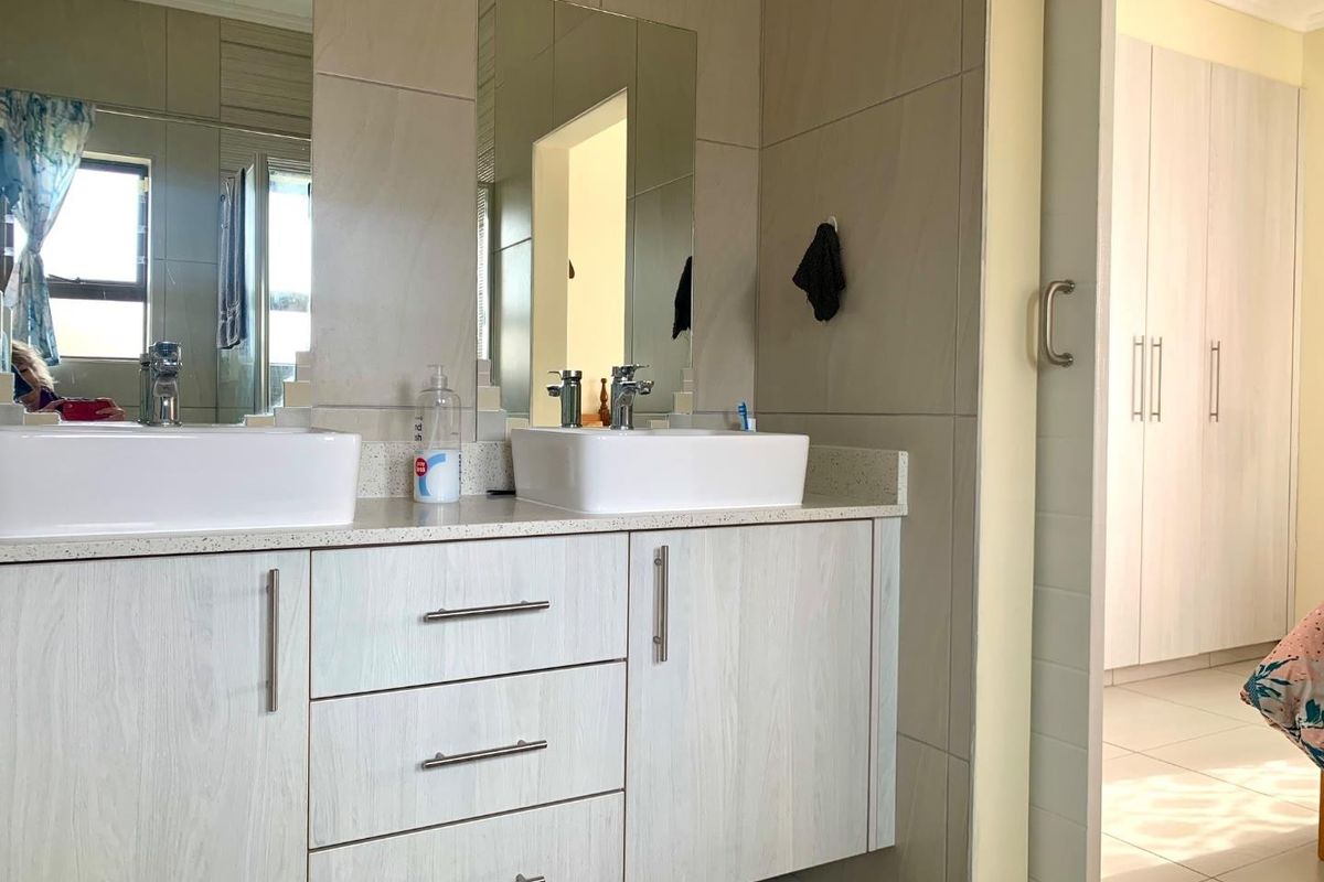 Modern bathroom featuring a double vanity with vessel sinks, stone countertop, built-in cabinetry, and neutral wall tiling.