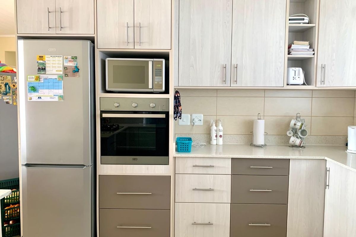A functional kitchen featuring light wood-grain cabinetry, integrated oven and microwave, stone-look countertops, and a neutral tiled backsplash.