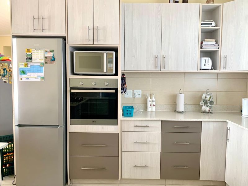 A functional kitchen featuring light wood-grain cabinetry, integrated oven and microwave, stone-look countertops, and a neutral tiled backsplash.