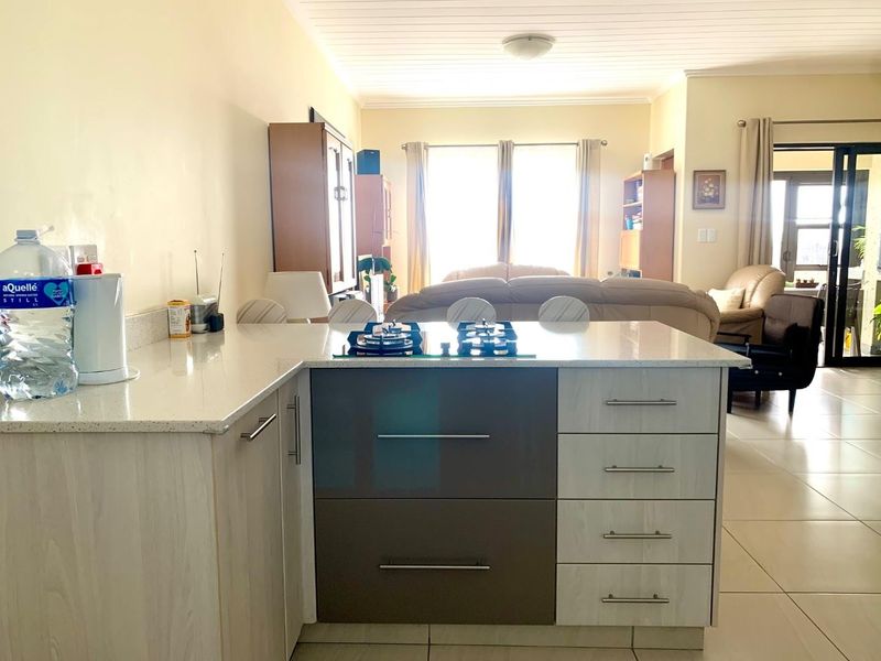 Open-plan living area featuring a modern kitchen island with a gas hob, stone countertops, and tiled flooring, flowing into a bright lounge space.