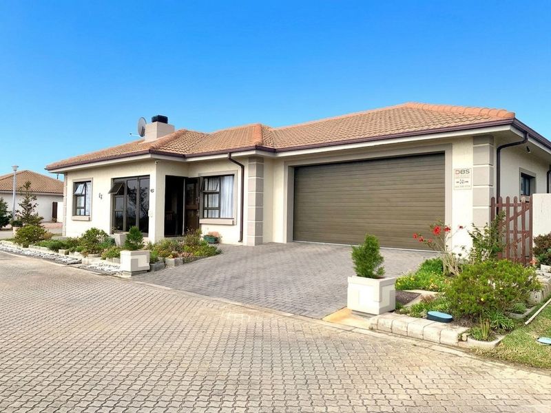 A well-maintained single-story residential property featuring a paved driveway, automated garage, and tiled roof, set within a neat landscaped environment.