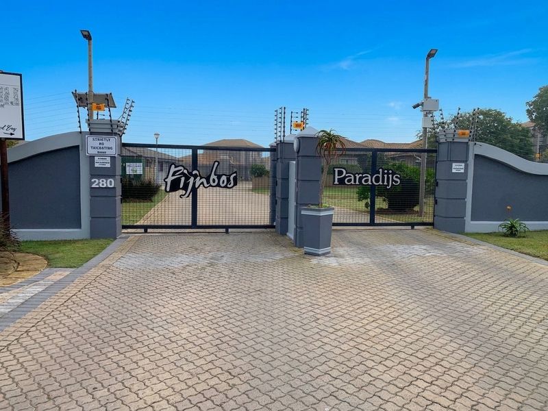 The entrance to Fijnbos Paradijs complex featuring a secure gated access point with electric fencing and paved driveway.