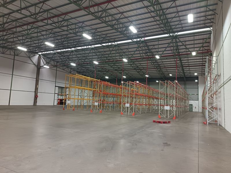 Spacious industrial warehouse featuring high-bay lighting, exposed steel roof trusses, durable concrete flooring, and extensive built-in steel racking systems.