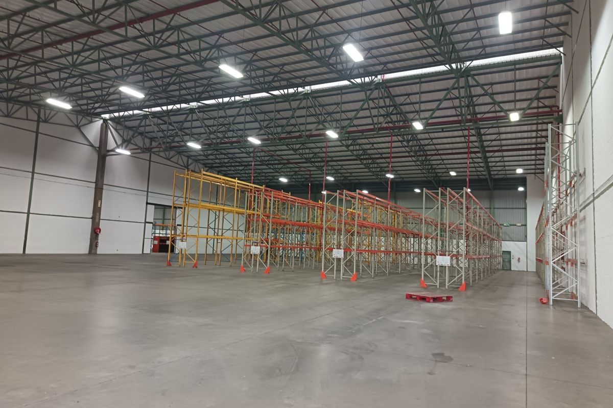 Spacious industrial warehouse featuring high-bay lighting, exposed steel roof trusses, durable concrete flooring, and extensive built-in steel racking systems.