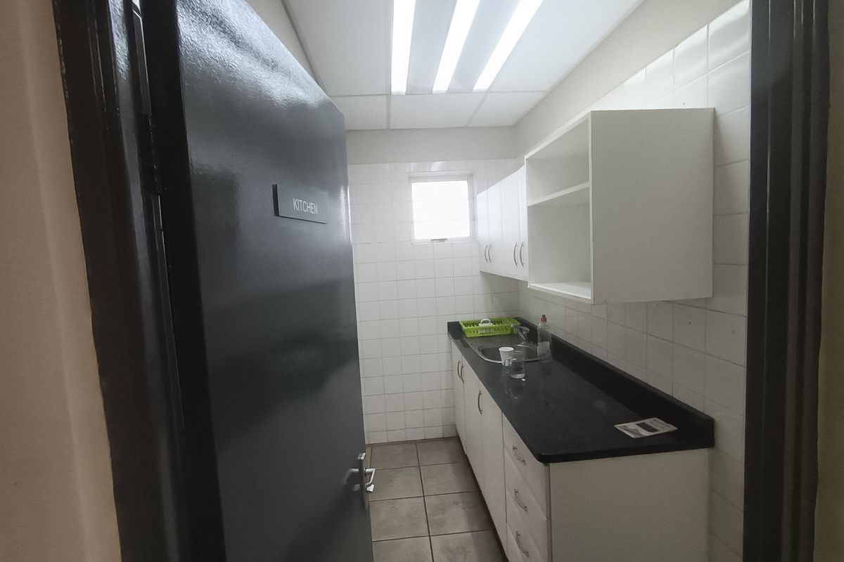 A functional industrial kitchen space featuring built-in cabinetry, a stainless steel sink, tiled splashbacks, and durable tiled flooring.