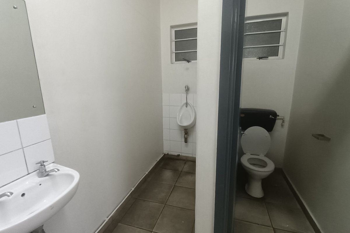 Functional industrial bathroom facility featuring a wall-mounted urinal, standard toilet, and pedestal washbasin with tiled flooring and splashbacks.