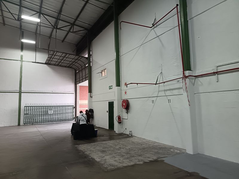 Spacious industrial warehouse unit featuring high ceilings with exposed steel trusses, concrete flooring, and integrated fire safety infrastructure including a hose reel and sprinklers.