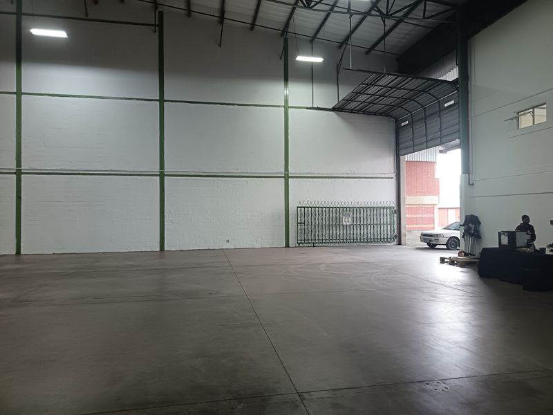 Spacious industrial warehouse unit featuring high ceilings with exposed steel trusses, durable concrete flooring, and a large roller shutter door for easy access.