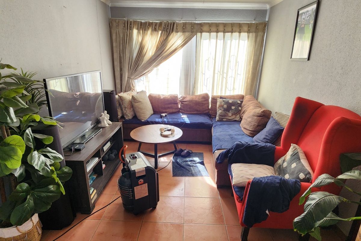 A cozy living room featuring tiled flooring and large windows with curtain rails, providing a functional space for relaxation.