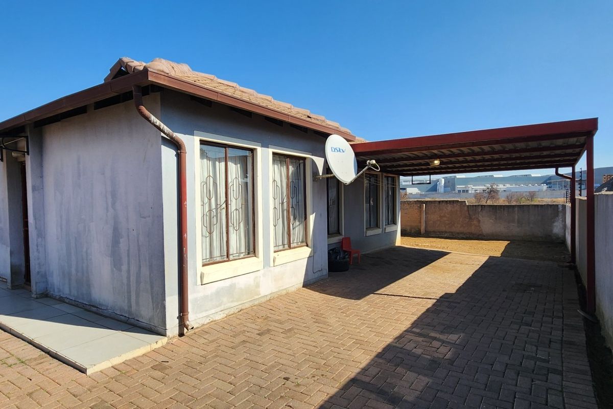 Rear view of the property featuring a paved driveway, attached carport, and perimeter boundary wall.