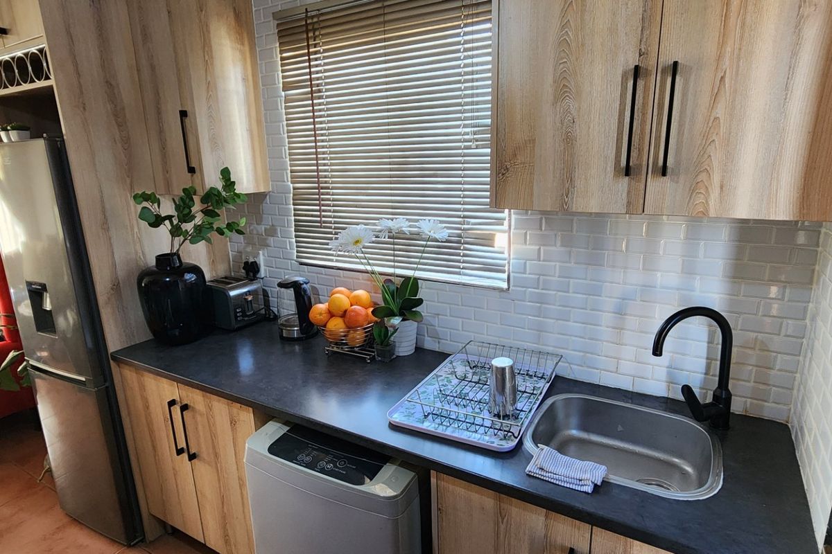 A modern kitchen featuring light wood-grain cabinetry, a white subway tile backsplash, dark countertops, and a sleek matte black faucet.