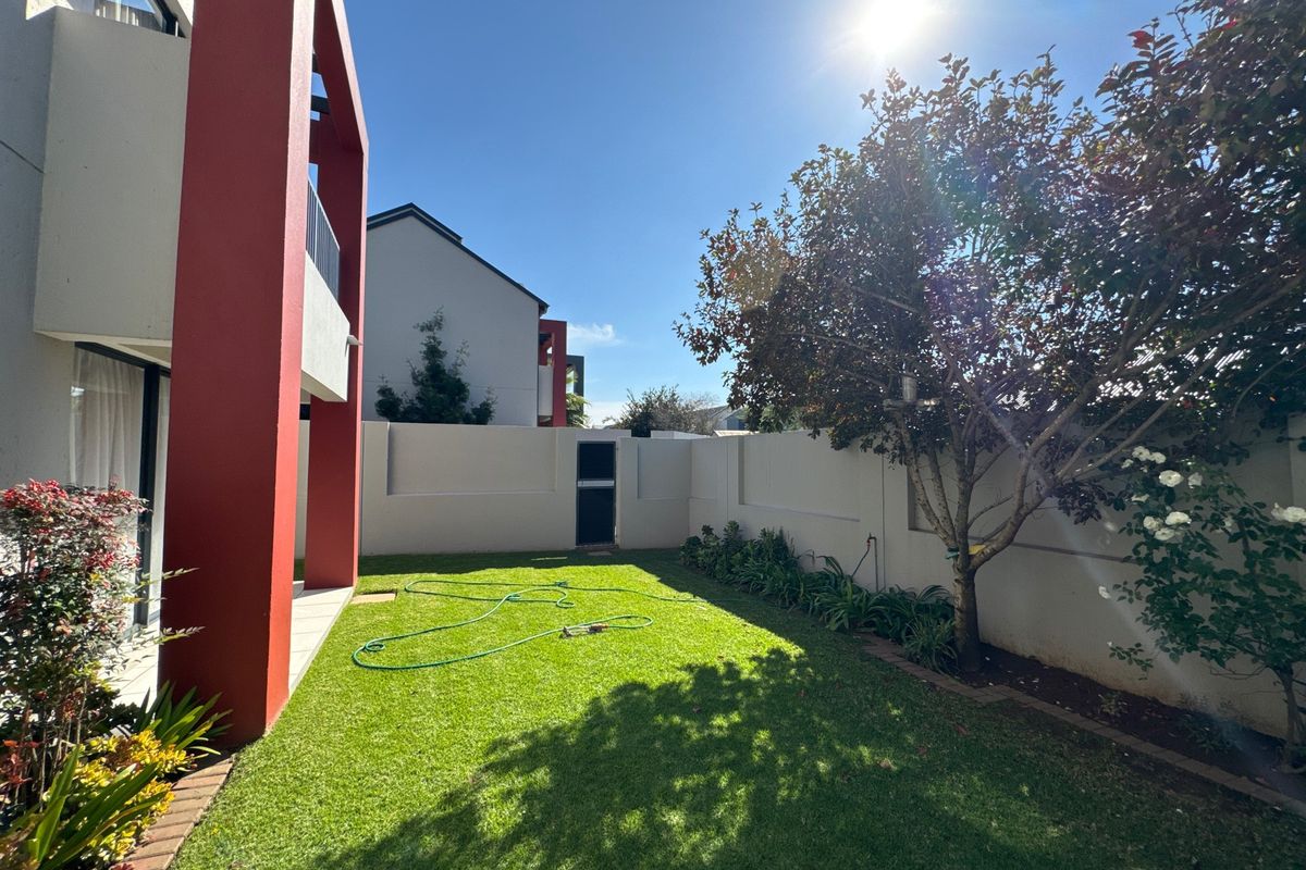 A well-maintained rear garden featuring a manicured lawn, perimeter boundary walls, and a paved patio area adjacent to the building structure.
