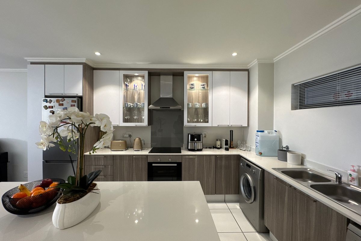 Modern kitchen featuring two-tone cabinetry, stone countertops, integrated appliances, and a functional layout with a central island and dedicated laundry space.