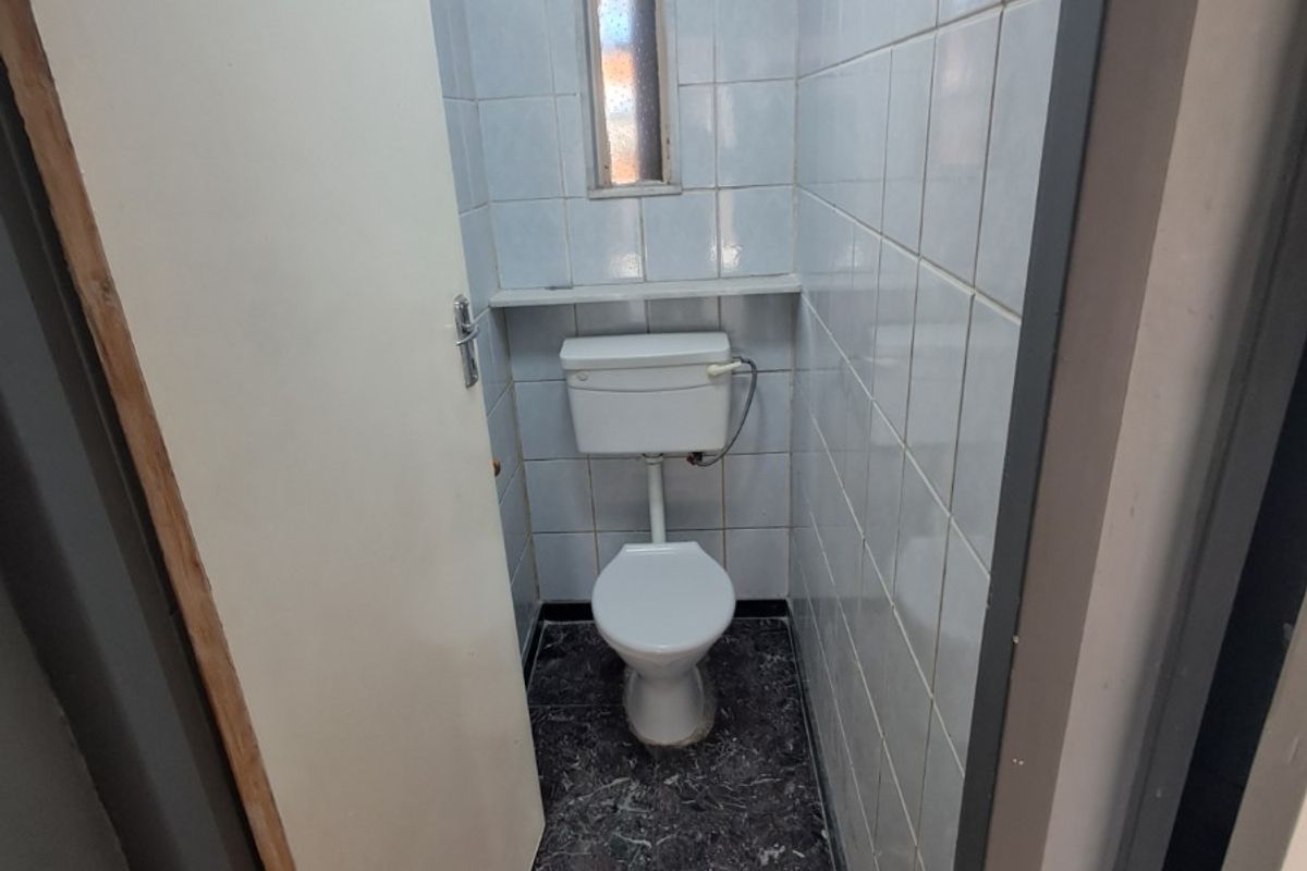 A compact, dated bathroom featuring a standard toilet, tiled walls, and dark stone-look flooring, suitable for a modern renovation.