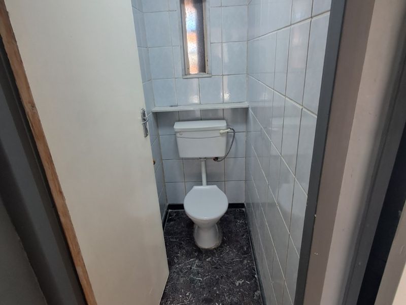A compact, dated bathroom featuring a standard toilet, tiled walls, and dark stone-look flooring, suitable for a modern renovation.