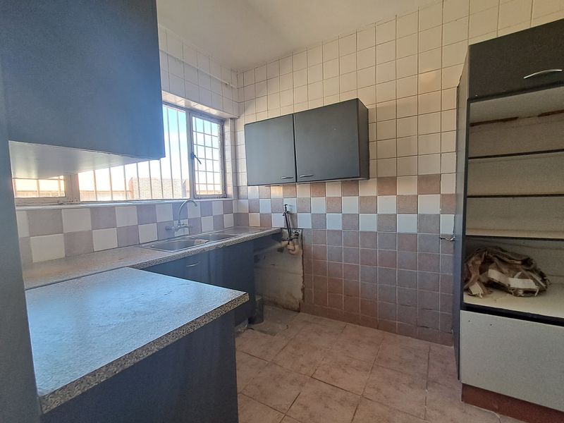 A dated kitchen featuring built-in cabinetry, a stainless steel sink, and tiled finishes, currently vacant and requiring cosmetic updates.