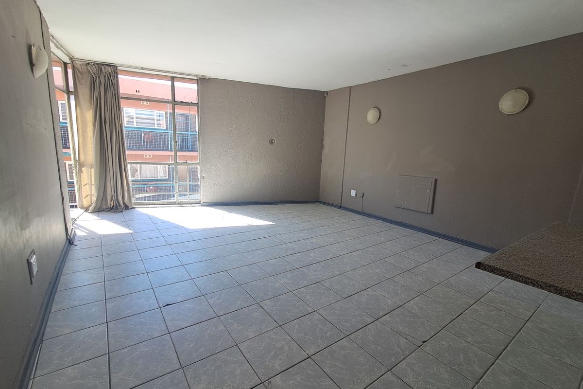 An empty, open-plan living area featuring tiled flooring, wall-mounted lighting, and large windows providing natural light.