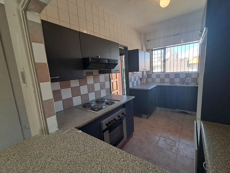 A functional kitchen featuring dark cabinetry, built-in oven and hob, tiled splashbacks, and a double sink, offering potential for modernization.