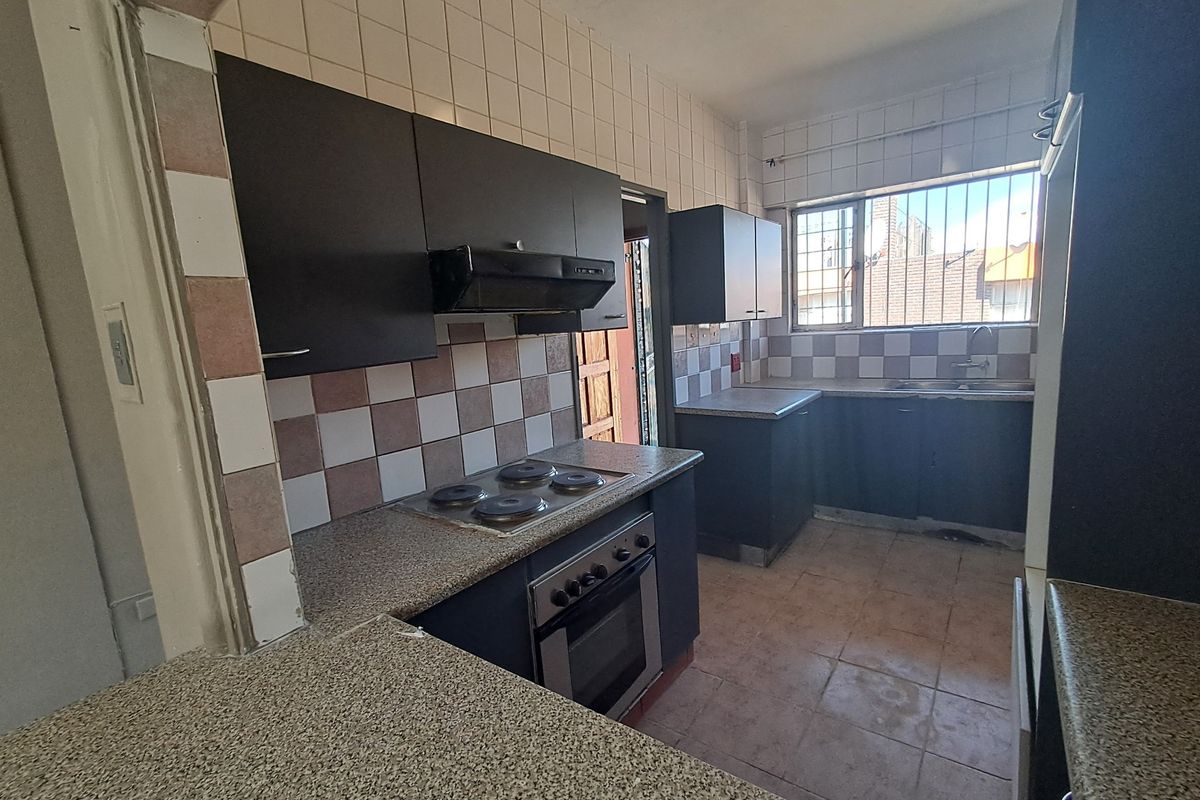 A functional kitchen featuring dark cabinetry, built-in oven and hob, tiled splashbacks, and a double sink, offering potential for modernization.