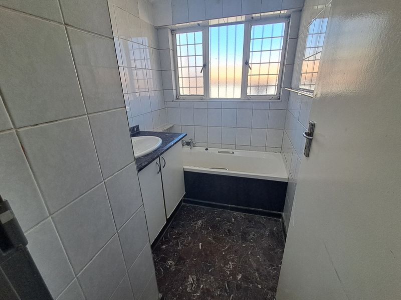 A compact bathroom featuring a built-in vanity with basin, a standard bathtub, and tiled finishes throughout, awaiting modern updates.