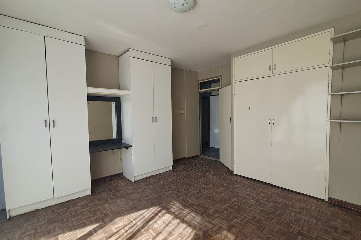 An empty bedroom featuring extensive built-in cupboard storage, a built-in vanity unit, and traditional parquet flooring.