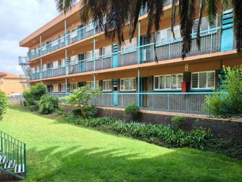 A multi-story apartment building exterior featuring brick facade, metal balcony railings, and a well-maintained communal garden area.