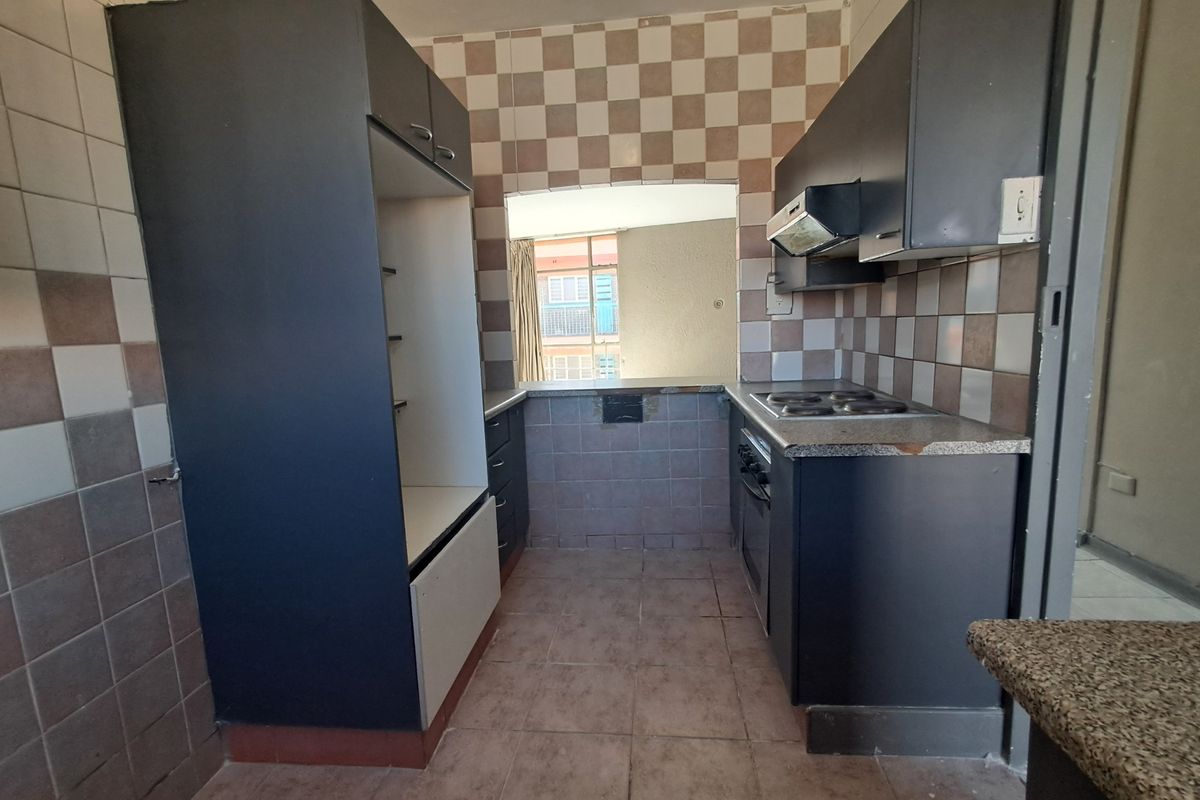 A compact kitchen featuring dark cabinetry, an electric hob, built-in oven, and a pass-through window, offering a functional layout ready for modernization.