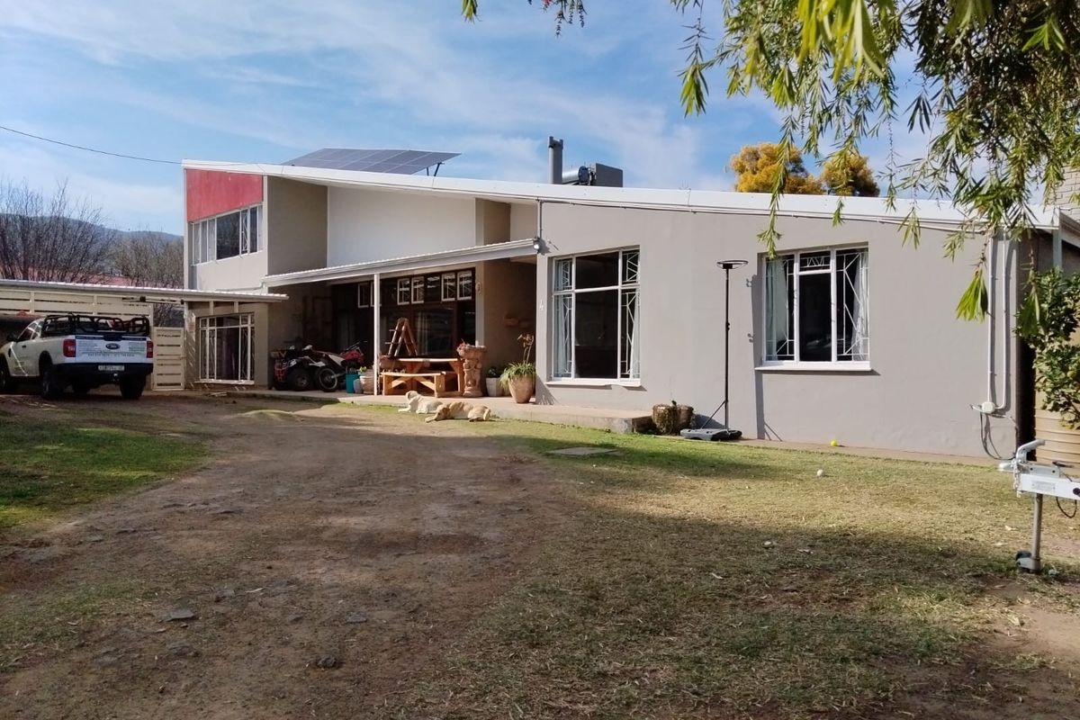 Rear view of a modern house featuring a covered patio, solar panels, and a spacious yard with an attached carport.