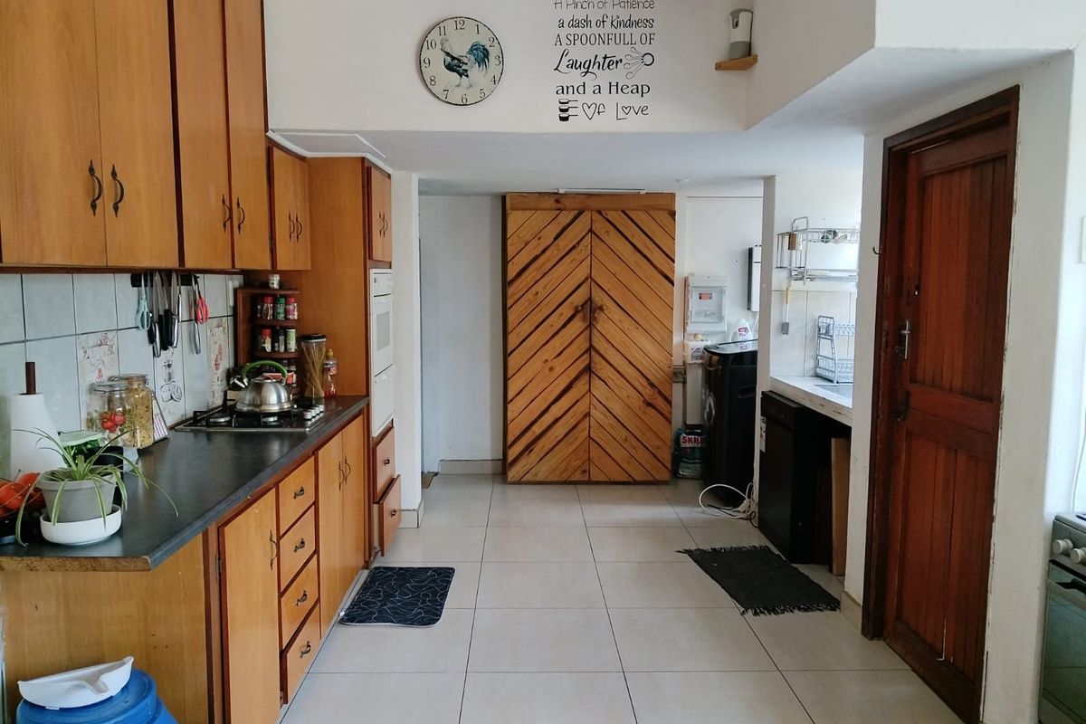 A functional kitchen featuring wooden cabinetry, tiled flooring, and a built-in oven and hob, offering a traditional layout with ample storage space.