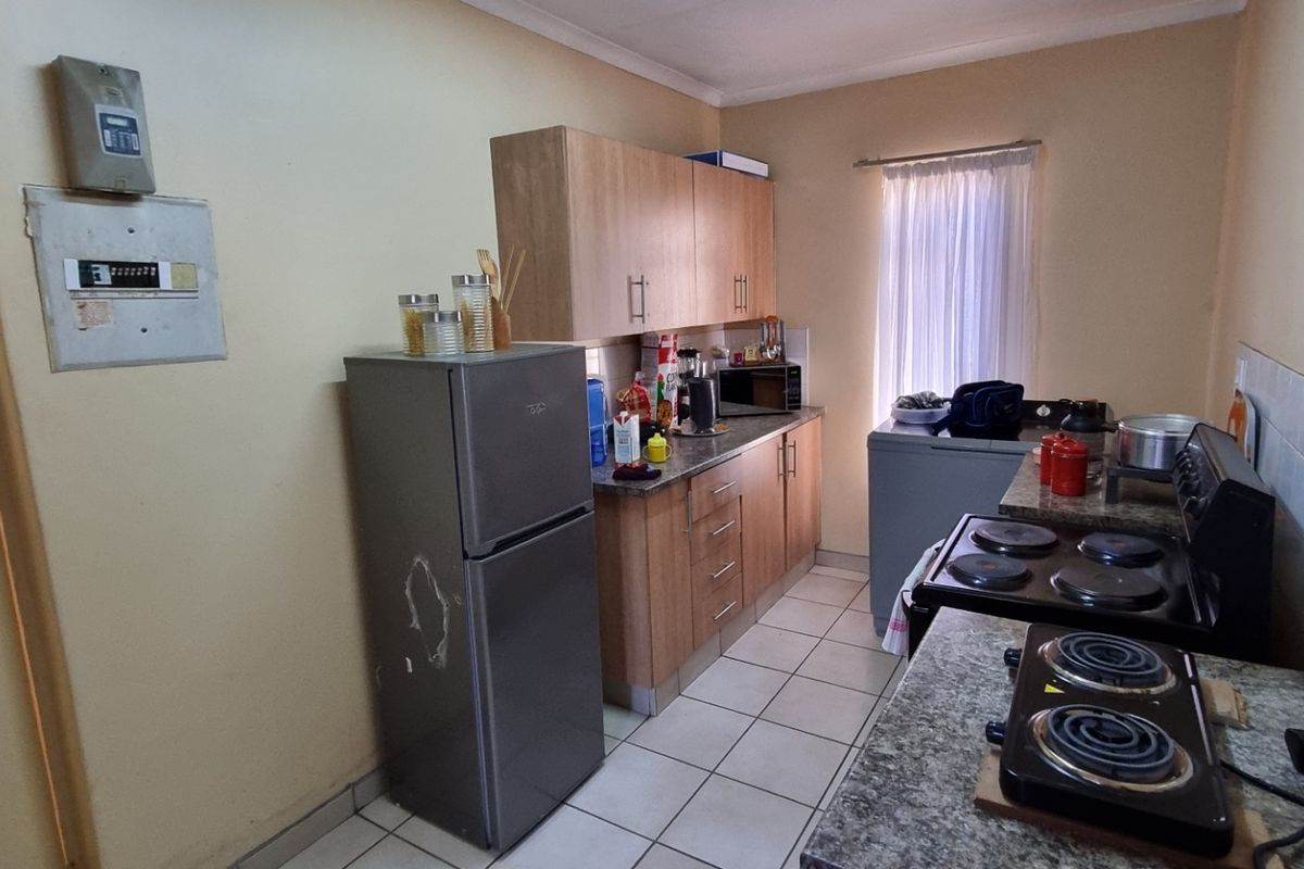 A functional kitchen featuring laminate cabinetry, granite countertops, and tiled flooring, offering a practical layout with potential for cosmetic updates.
