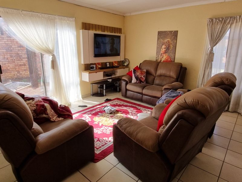 A comfortable living room featuring tiled flooring, a built-in media unit, and large sliding glass doors providing access to the exterior.