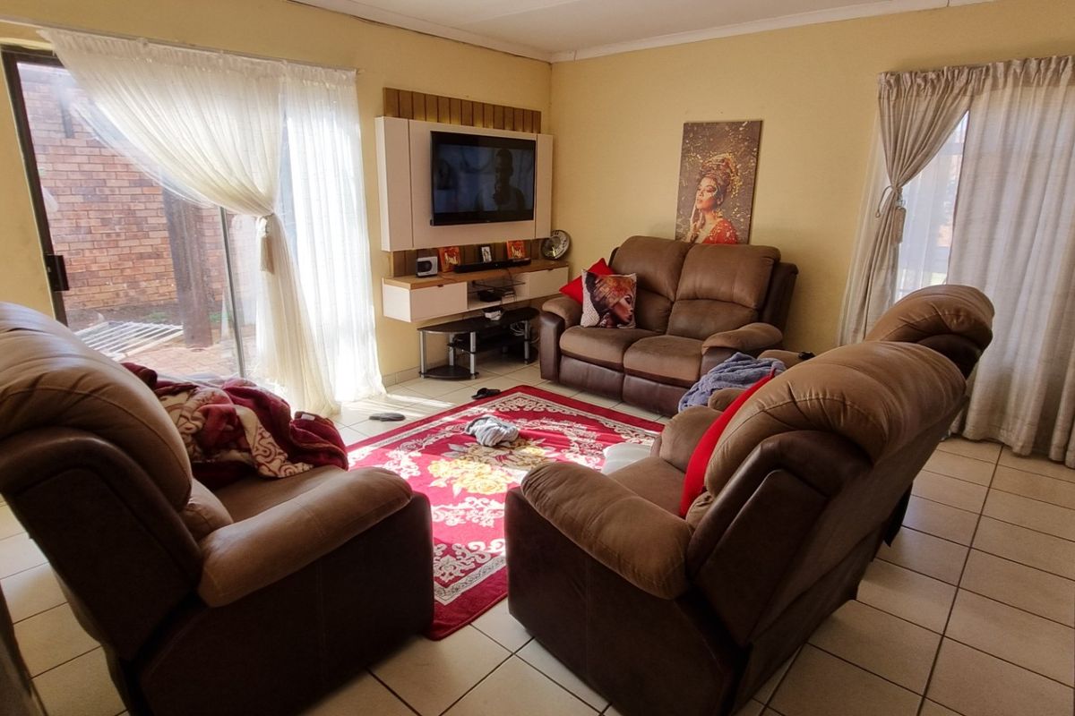 A comfortable living room featuring tiled flooring, a built-in media unit, and large sliding glass doors providing access to the exterior.