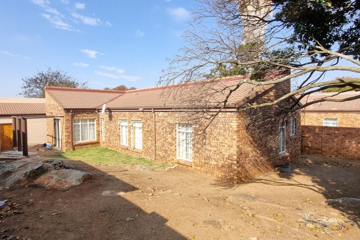 Rear view of a face brick house featuring a tiled roof, perimeter walling, and an expansive, unlandscaped garden area.
