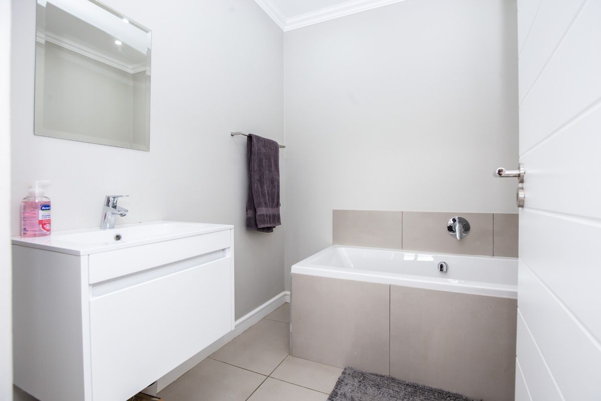 A modern, well-maintained bathroom featuring a sleek white vanity, wall-mounted mirror, and a tiled built-in bathtub with contemporary fixtures.