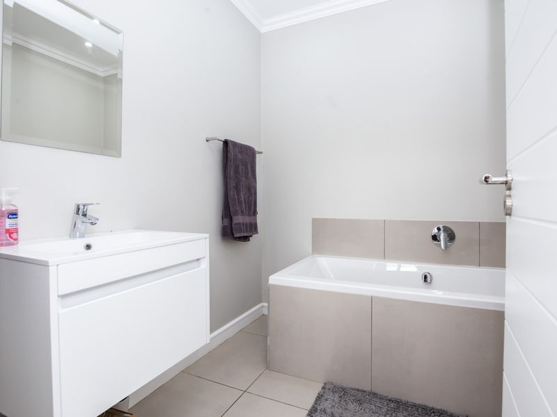 A modern, well-maintained bathroom featuring a sleek white vanity, wall-mounted mirror, and a tiled built-in bathtub with contemporary fixtures.