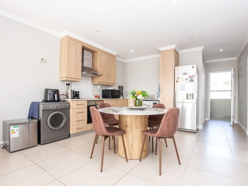 Open-plan kitchen and dining area featuring light wood cabinetry, modern tiled flooring, and a clean, functional layout with integrated appliances.