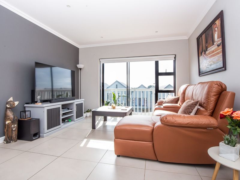 A bright and modern living room featuring large sliding glass doors that open to a balcony, complemented by neutral tiled flooring and recessed lighting.
