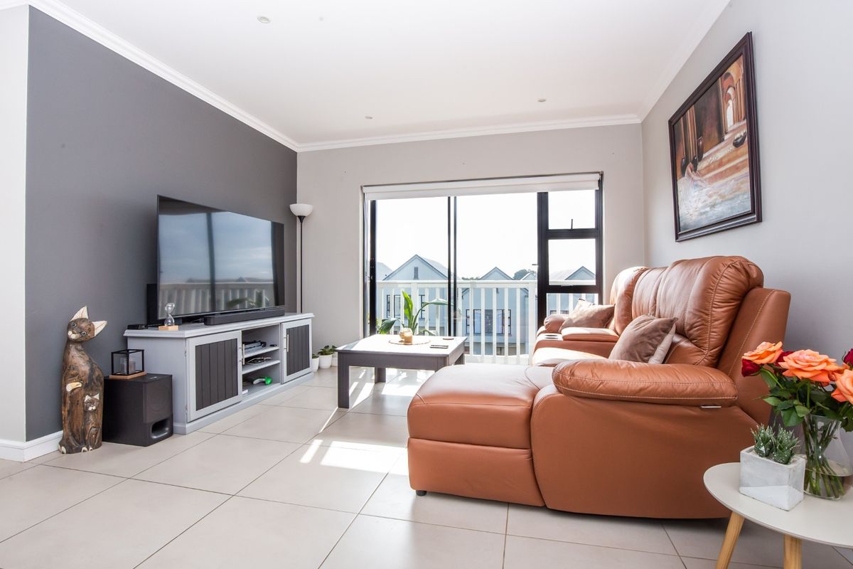 A bright and modern living room featuring large sliding glass doors that open to a balcony, complemented by neutral tiled flooring and recessed lighting.