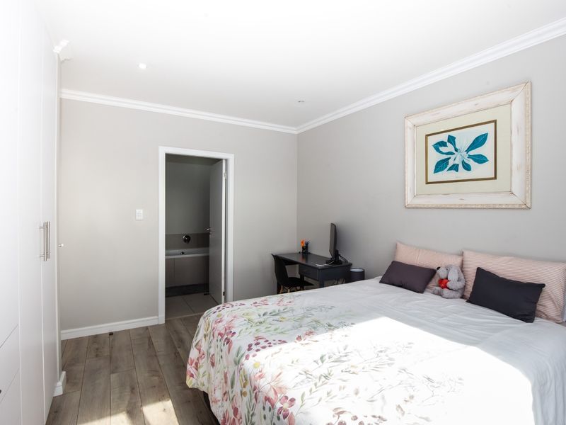 A well-maintained bedroom featuring modern laminate flooring, built-in cupboards, and neutral wall finishes with direct access to an en-suite bathroom.