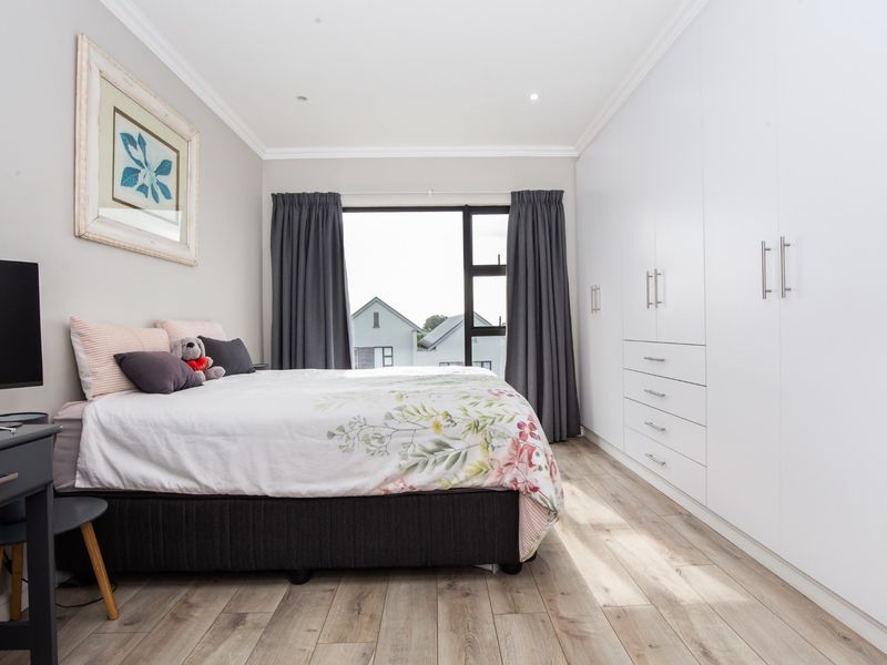 A well-maintained bedroom featuring extensive built-in floor-to-ceiling cupboards, modern laminate flooring, and neutral finishes with natural light.