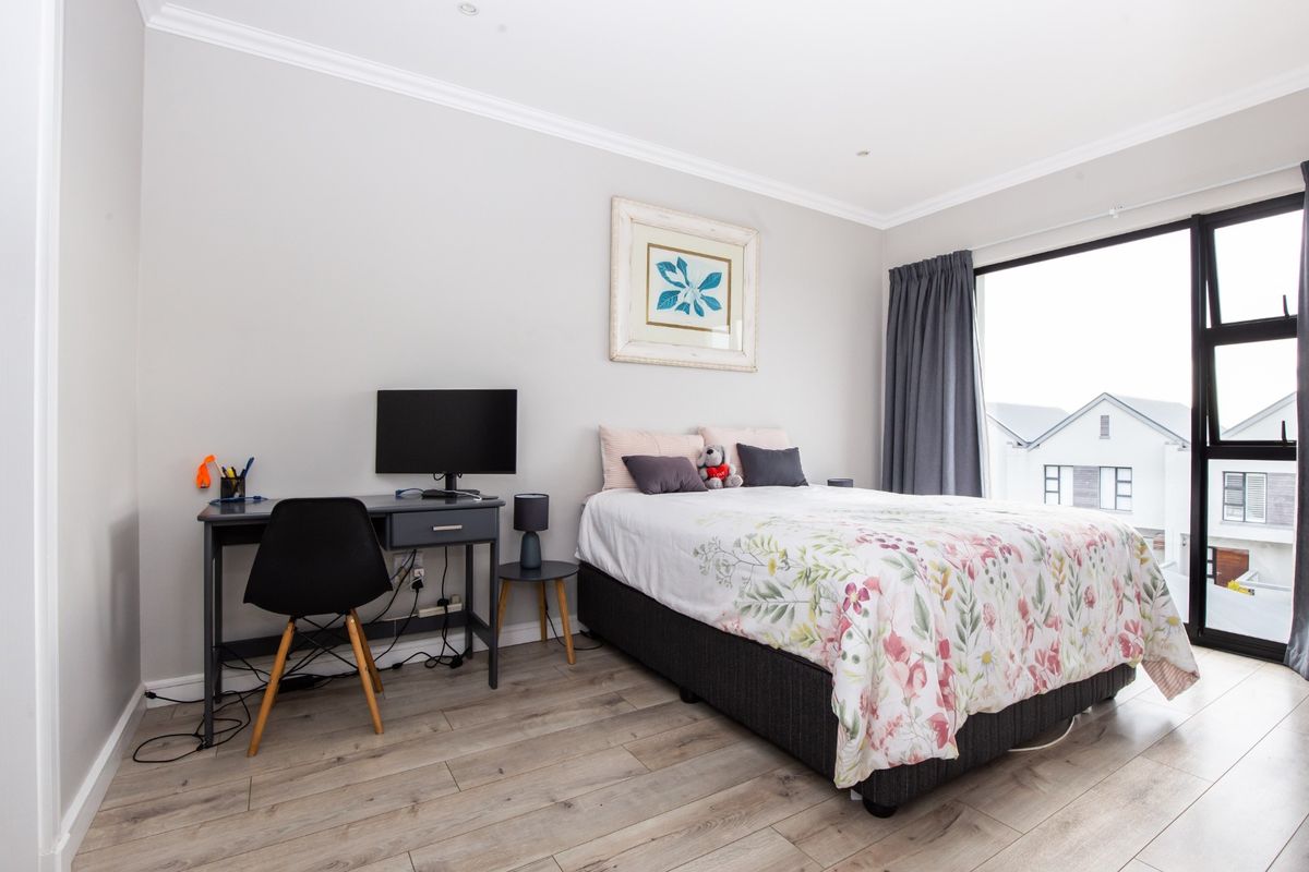 A well-maintained bedroom featuring light-toned laminate flooring, recessed ceiling lighting, and a large sliding glass door providing natural light and exterior views.