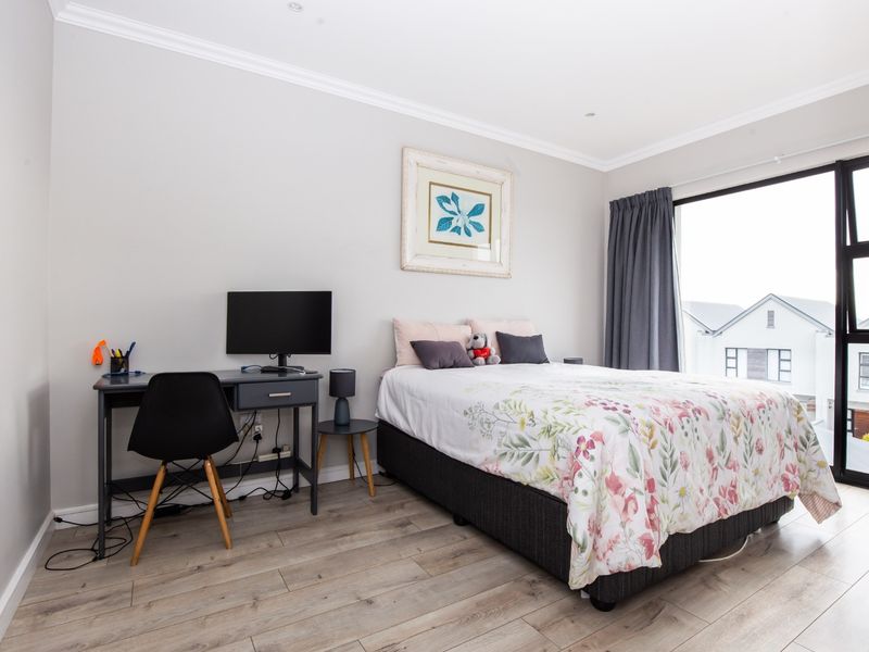 A well-maintained bedroom featuring light-toned laminate flooring, recessed ceiling lighting, and a large sliding glass door providing natural light and exterior views.
