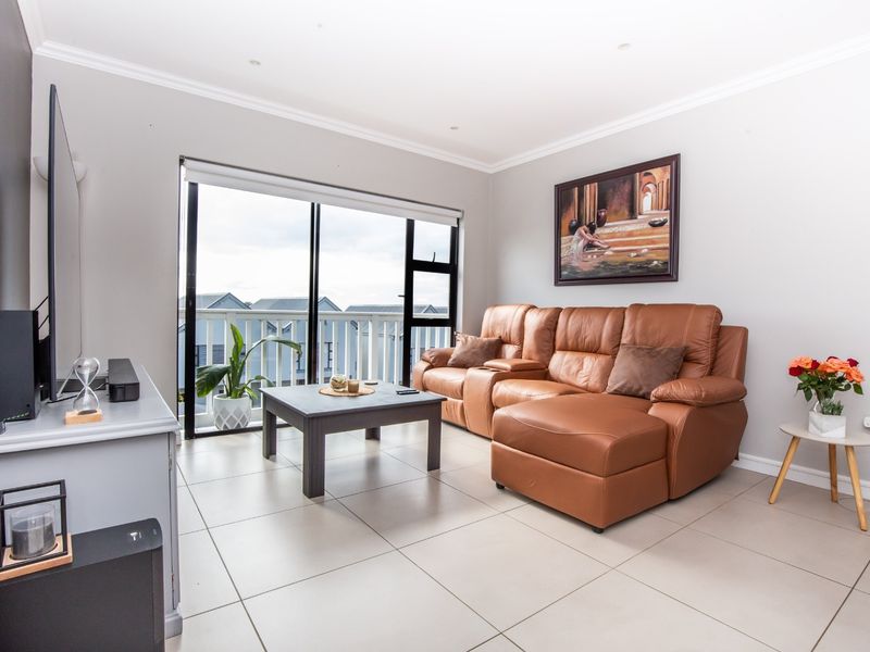 A bright and well-maintained living room featuring large sliding glass doors that open onto a balcony, with neutral tiled flooring and recessed lighting.