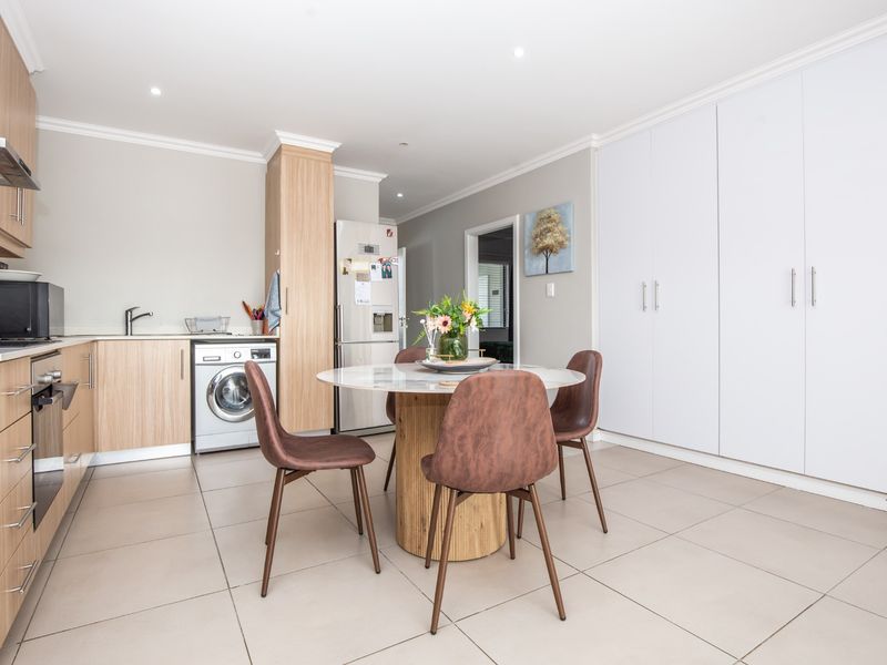 Modern open-plan kitchen and dining area featuring light wood cabinetry, integrated appliances, tiled flooring, and ample built-in storage cupboards.
