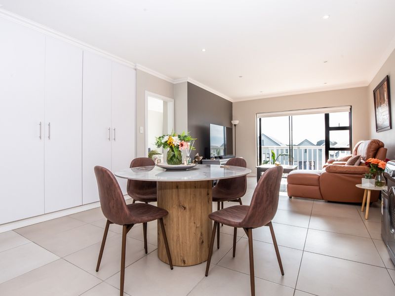Spacious open-plan living and dining area featuring neutral tiled flooring, ample built-in storage, and seamless access to a private balcony.